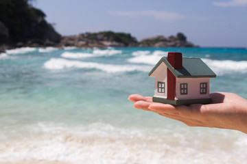someone holding a tiny house in front of the ocean