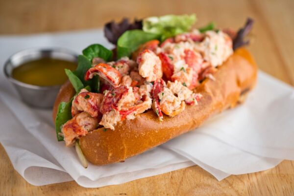 A lobster roll with a cup of sauce.